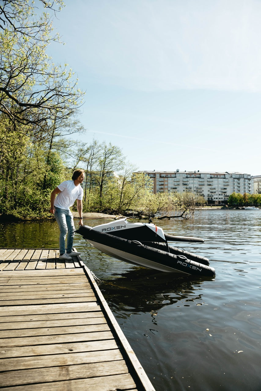 Man standing on a wooden dock next to an inflatable jetski on a lake