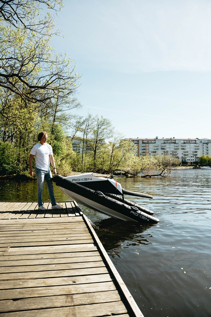 Man standing on a wooden dock next to an inflatable jetski on a lake