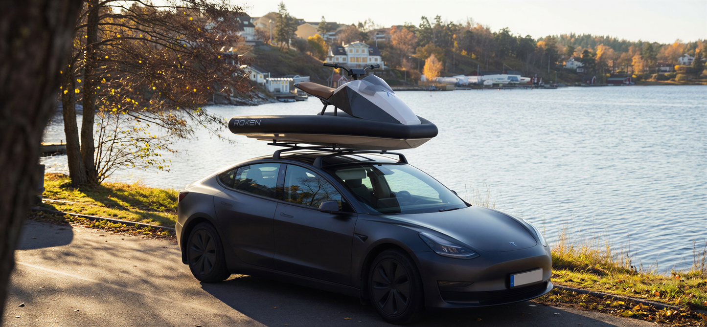 Car with a roof rack carrying a jet ski by a lakeside.